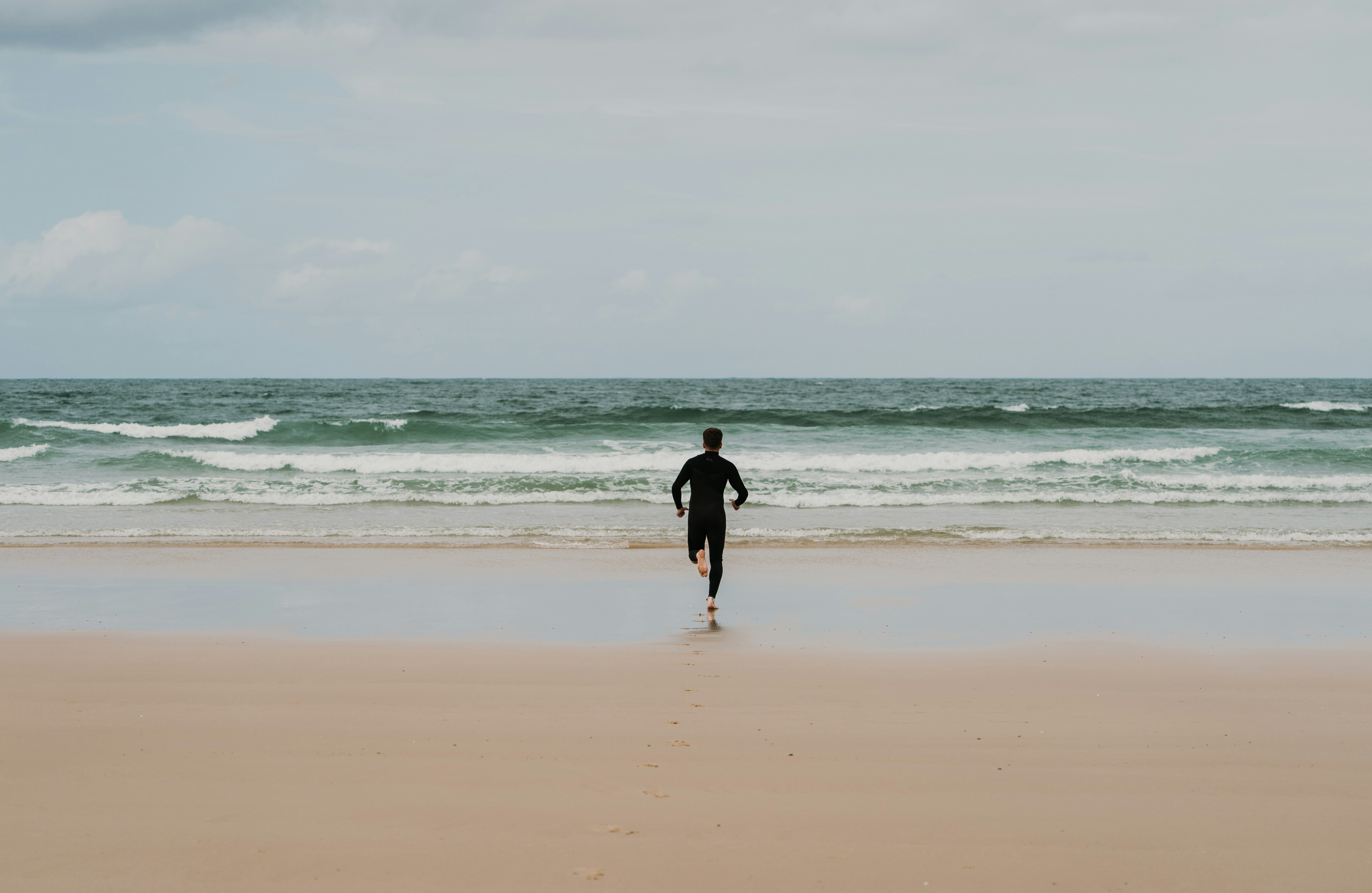 man in black shirt walking on beach during daytime